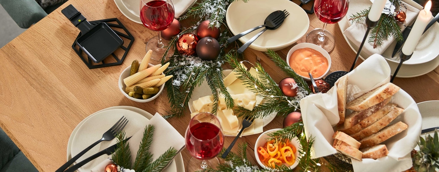 Festlicher Esstisch von Möbel Gruber mit Rotwein, Brot, Käse, Gurken, Cornichons und Weihnachtsdekoration.