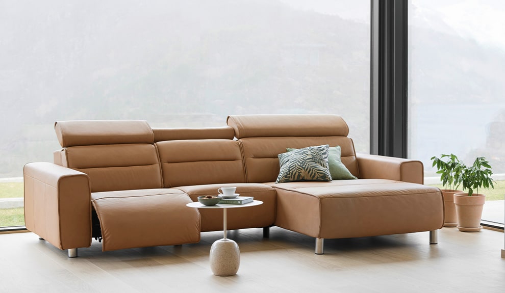 Ein modernes Wohnzimmer, eingerichtet von Möbel Gruber, mit einem braunen Ledersofa, einem runden Tisch mit Kaffeetassen und einer Topfpflanze.