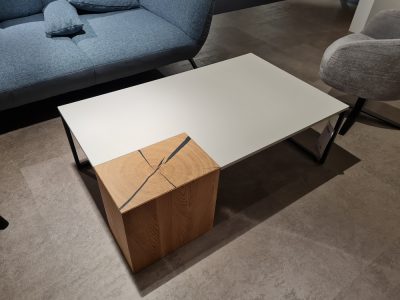 Ein moderner Couchtisch mit Holz- und weißen Elementen steht zwischen einem blauen und einem grauen Stuhl.