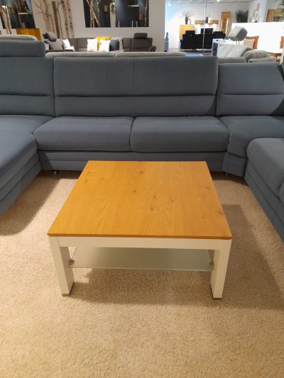 Der Couchtisch ruht auf einem beigen Teppich, umgeben von einem großen blauen Sofa im Showroom von Möbel Gruber.