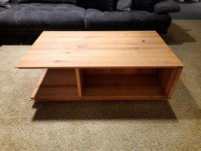 Couchtisch von Möbel Gruber mit zwei Ablageflächen auf beigem Teppich, umrahmt von einem dunklen Sofa.
