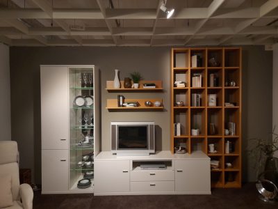 Wohnwand von Möbel Gruber: ein modernes Wohnzimmer mit weißer Entertainment-Einheit, Deko-Regalen und Fernseher. Gemütliches, stilvolles Design.
