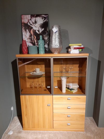 Der Highboard-Holzschrank mit Glastüren präsentiert Geschirr, Gläser und Bücher und ist mit Vasen und Kunstwerken akzentuiert.