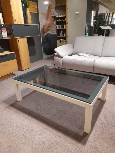 Ein Wohnzimmer von Möbel Gruber mit einem Musterring Couchtisch, beigem Sofa, Holzregalen und einem großen abstrakten Wandposter.