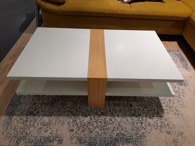 Couchtisch von Möbel Gruber, modernes Weiß mit Holzstreifen, auf einem gemusterten Teppich neben einem senfgelben Sofa.
