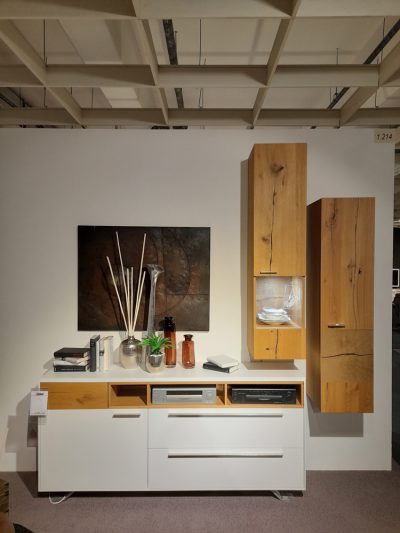 Zeitgenössisches Wohnzimmer von Möbel Gruber mit Interliving-Sideboard, Holz-/Weißschränken, abstrakter Wandkunst und Dekorationsartikeln.
