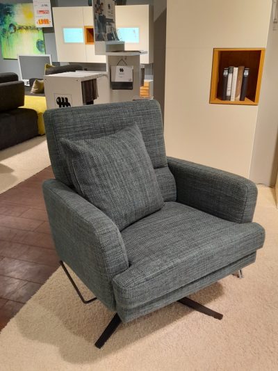 Ein Musterring-Einzelsessel mit passendem Kissen steht auf einem beigen Teppich im modernen Showroom von Möbel Gruber.