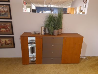 Ein Musterring-Holz-Sideboard mit Schubladen, Pflanzen und Büchern lehnt an einer weißen Wand mit gerahmten Bildern.
