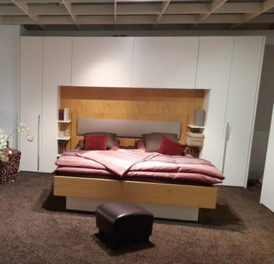 Schlafzimmer von Möbel Gruber: Doppelbett, weiße Schränke, Holzakzente, braune Bettwäsche und Ottomane auf Teppich.