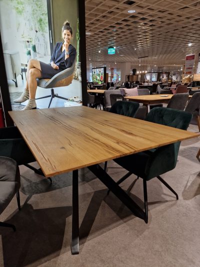 Ein Esstisch mit dunklen Metallbeinen, grünen Stühlen und einem Möbel Gruber-Poster im Showroom.