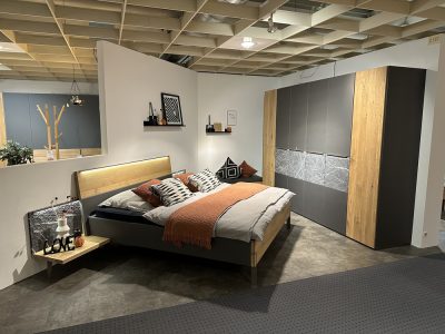 Modernes Schlafzimmer mit einem Schlafzimmerbett, gemusterten Kissen, einer orangefarbenen Überdecke und einem großen Kleiderschrank auf gefliestem Boden.