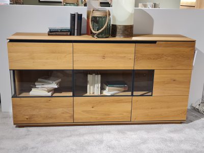 Das Sideboard präsentiert Bücher mit Dekor darauf und verfügt über Glasabschnitte, die auf einem mit Teppich ausgelegten Boden ruhen.