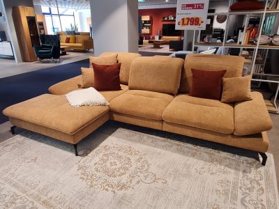 Eine Polstergarnitur mit braunen Kissen und einer weißen Überdecke auf einem Teppich im Showroom von Möbel Gruber.