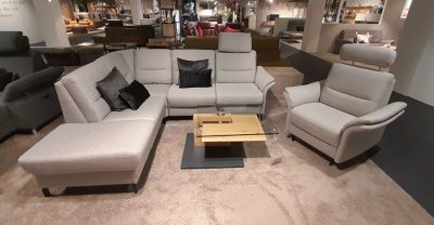 Ausstellungsraum von Möbel Gruber: Polstergarnitur mit Sessel mit grauem Sofa, Sessel, Couchtisch aus Holz und schwarzen Kissen.