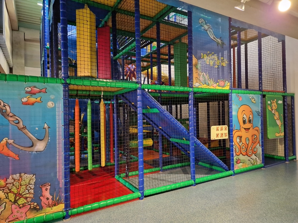 Indoor-Spielplatz mit farbenfrohen Klettergerüsten, Rutschen und Netzen. Mit Wandgemälden zum Thema Ozean dekoriert.