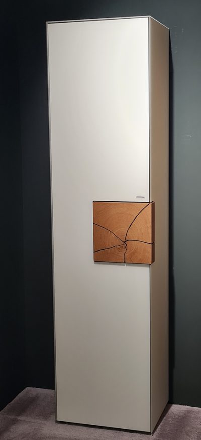 Das Hartmann Standelement ist ein hoher weißer Schrank mit Holzgriff, ideal für dunkle Ecken auf einem grauen Teppich.