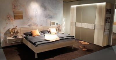 Modernes Schlafzimmer mit Holzbett, grauer Bettwäsche, orangefarbenen Kissen, einem Kleiderschrank mit Schiebetüren von Möbel Gruber und Wandkunst.