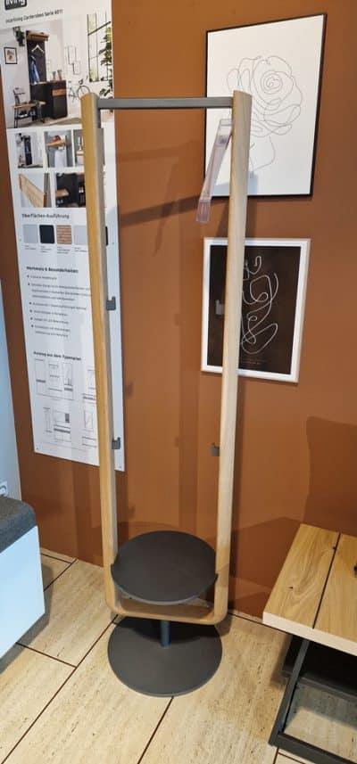 Der Voglauer Stummer Diener wird mit Regalen, Wandkunst und Postern an einer schicken braunen Showroomwand bei Möbel Gruber präsentiert.