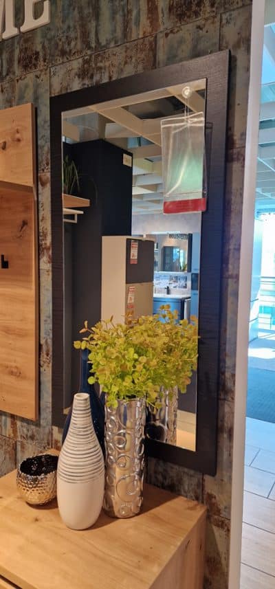 Ein Spiegel Wandspiegel mit schwarzem Rahmen, Pflanze in silberner Vase und zwei Vasen von Möbel Gruber auf Holzoberfläche.