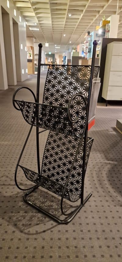 Der Zeitungsständer von Möbel Gruber, ein schwarzer Zeitschriftenständer aus Metall mit geometrischen Mustern, schmückt den mit Teppich ausgelegten Raum.