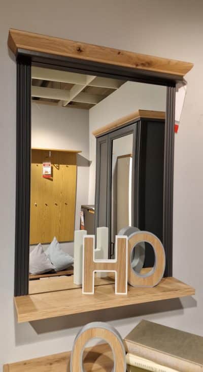 Ein Spiegel mit Holzablage zeigt die Buchstaben „H“ und „O“ in einem modernen Innenraumambiente.