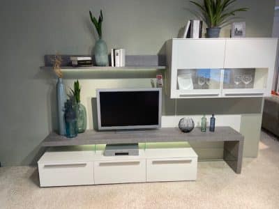 Wohnwand von Möbel Gruber: TV-Set mit weißen Schränken, Vasen, Büchern und Pflanzen auf Regalen.