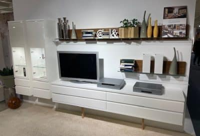 Modernes Wohnzimmer mit Regalen von Möbel Gruber, Fernseher und Deko wie Vasen und Büchern. In Vitrinen sind dekorative Objekte ausgestellt.