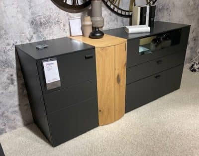 Musterring Sideboard von Möbel Gruber in Schwarz und Holz mit Schubladen und Vasen an einer strukturierten Wand und Teppichboden.