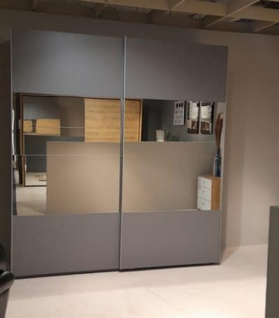 Der Schwebetürenschrank mit Spiegeltüren spiegelt einen gemütlichen Raum mit einer Holzkommode und Dekorationsgegenständen wider.