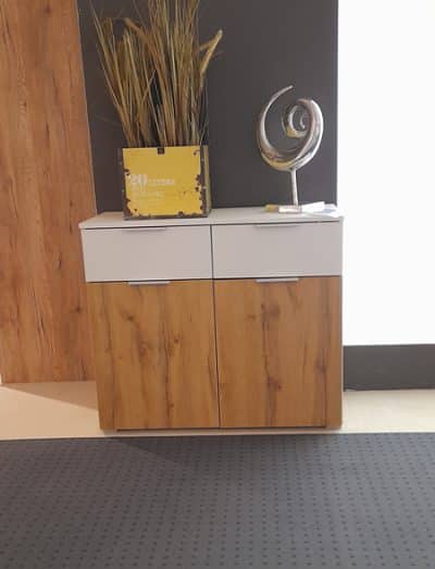 Der Holzschrank Kommode von Möbel Gruber hat zwei Schubladen, zwei Türen und ist mit einer Skulptur und getrockneten Pflanzen verziert.