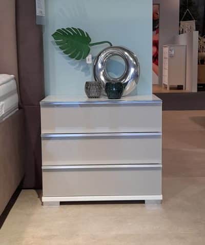 Nachtkonsole mit drei Schubladen, dekoriert mit Vasen und einer Metallskulptur, im Showroom von Möbel Gruber.