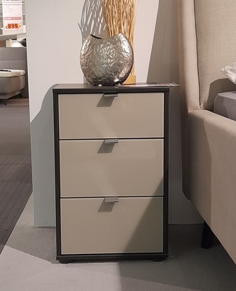 Das Nachtkonsolen-Paar von Möbel Gruber: ein moderner Nachttisch mit drei Schubladen neben einem beige gepolsterten Bett mit einer silbernen Vase.