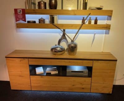 Interliving Sideboard mit Wandboard mit dekorativen Vasen, Regalen darüber und braunen und silbernen Akzenten.