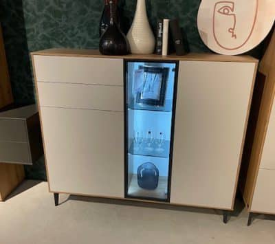 Ein modernes Interliving-Highboard mit einer Glasvitrine, Weingläsern, einem gerahmten Bild und dekorativen Vasen darauf.