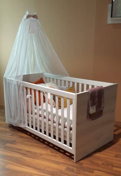 Foto vom einem weißen Kinderbett mit Schleier am Kopfbereich