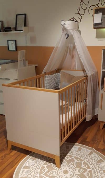 Foto vom einem braun/weißen Kinderbett mit Schleier am Kopfbereich