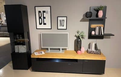 Das moderne Wohnzimmer von Möbel Gruber verfügt über die Wohnwand mit einem Fernseher, schwarzen Regalen, Dekor und gerahmten Zitaten an der Wand.