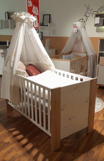 Foto vom einem braun/weißen Kinderbett mit Schleier am Kopfbereich