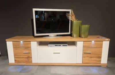 Ein modernes TV-Unterteil von Möbel Gruber mit Flachbildfernseher, Vasen und beleuchteten Regalen vor dunklem Hintergrund.