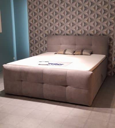 Das Boxspringbett mit Bettkasten von Möbel Gruber ist ein grau gepolstertes Bett mit gepolstertem Kopfteil in einem modernen Schlafzimmer.