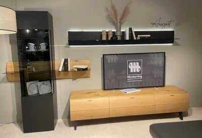 Modernes Wohnzimmer mit Musterring Wohnwand bestehend aus hölzernem Fernsehschrank, schwarzer Vitrine, Dekoregal und wandmontiertem Fernseher.