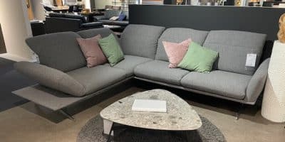Polstergarnitur mit rosa und grünen Kissen neben einem dreieckigen Couchtisch in einem Ausstellungsraum von Möbel Gruber.