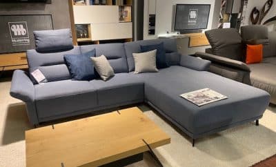 Musterring Polstergarnitur präsentiert ein graues Sofa mit Kissen, einen Couchtisch aus Holz und eine Zeitschrift in einem modernen Ambiente.