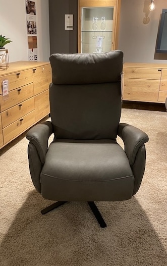Ein Lounge-Relaxsessel von Möbel Gruber steht auf einem beigen Teppich zwischen Holzschränken in einem sanft beleuchteten Raum.