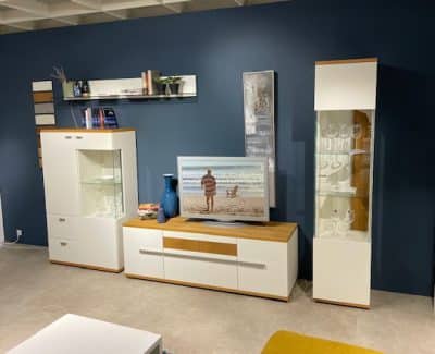 Modernes Wohnzimmer mit weißer Wohnwand von Möbel Gruber, einer Strandszene im Fernsehen und Dekor vor einer dunkelblauen Wand.