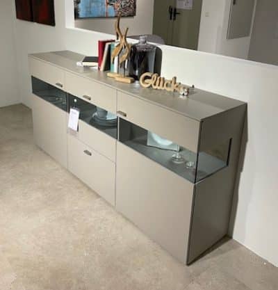 Das moderne graue Sideboard von Möbel Gruber wertet einen minimalistischen Raum mit seinen Glasfächern für Bücher und Dekoration auf.