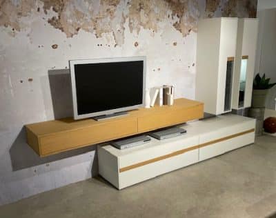 Die Wohnwand von Möbel Gruber verfügt über einen Flachbildfernseher auf einer Holzkonsole, weiße Schränke und eine strukturierte Wand im Wohnzimmer.
