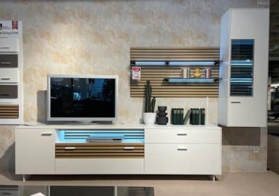 Moderne Wohnzimmereinrichtung mit Wohnwand von Möbel Gruber mit Fernseher, Wandregalen und Pflanzen vor einer strukturierten beigen Wand.