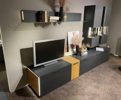 Interliving Wohnwand-Wohnzimmer mit Wandregal, Fernseher, dunklen Holzschränken und Dekor auf Teppichboden.