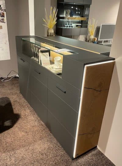 Das Interliving Highboard in modernem Grau von Möbel Gruber verfügt über eine Vitrine, Dekor auf der Oberseite und beleuchtete Kanten.